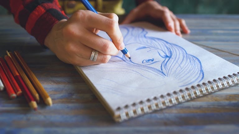 A person drawing on a notebook with pencils