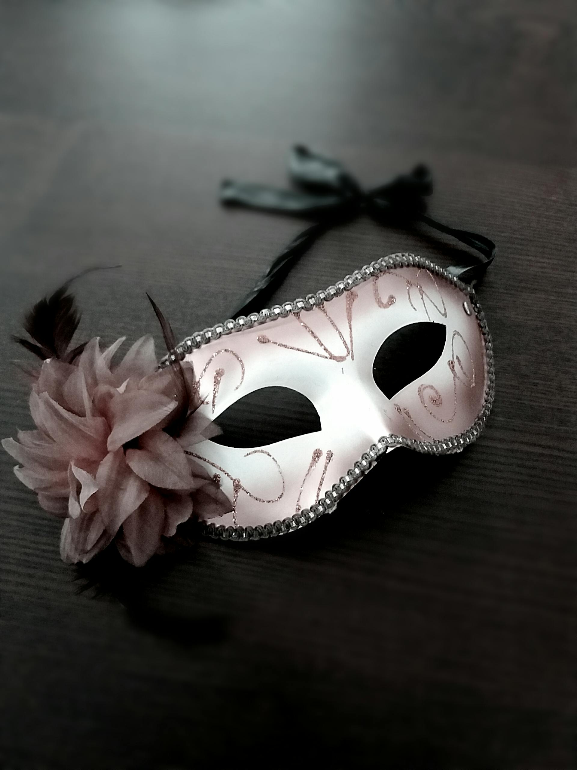 A beautiful Venetian masquerade mask with floral and feather details on a dark wooden table.