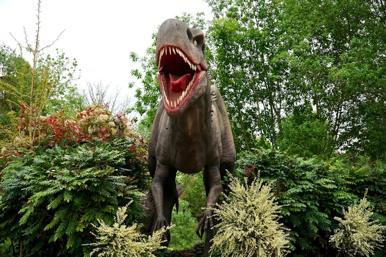 A lifelike dinosaur model surrounded by vibrant greenery in a tranquil park garden.