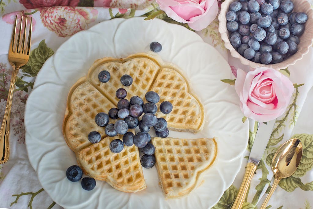 Delicious heart-shaped waffles topped with fresh blueberries and surrounded by pink roses.