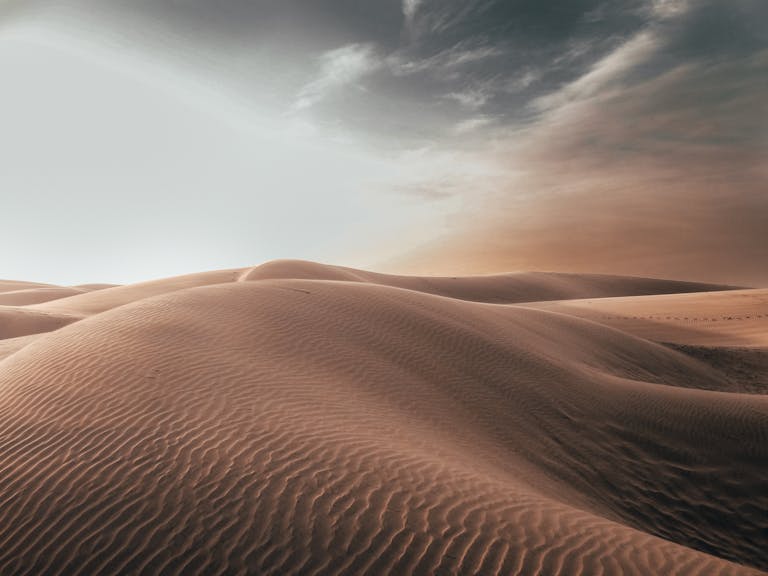 Majestic sand dunes under a dramatic sky, capturing the serenity of the desert at dawn.