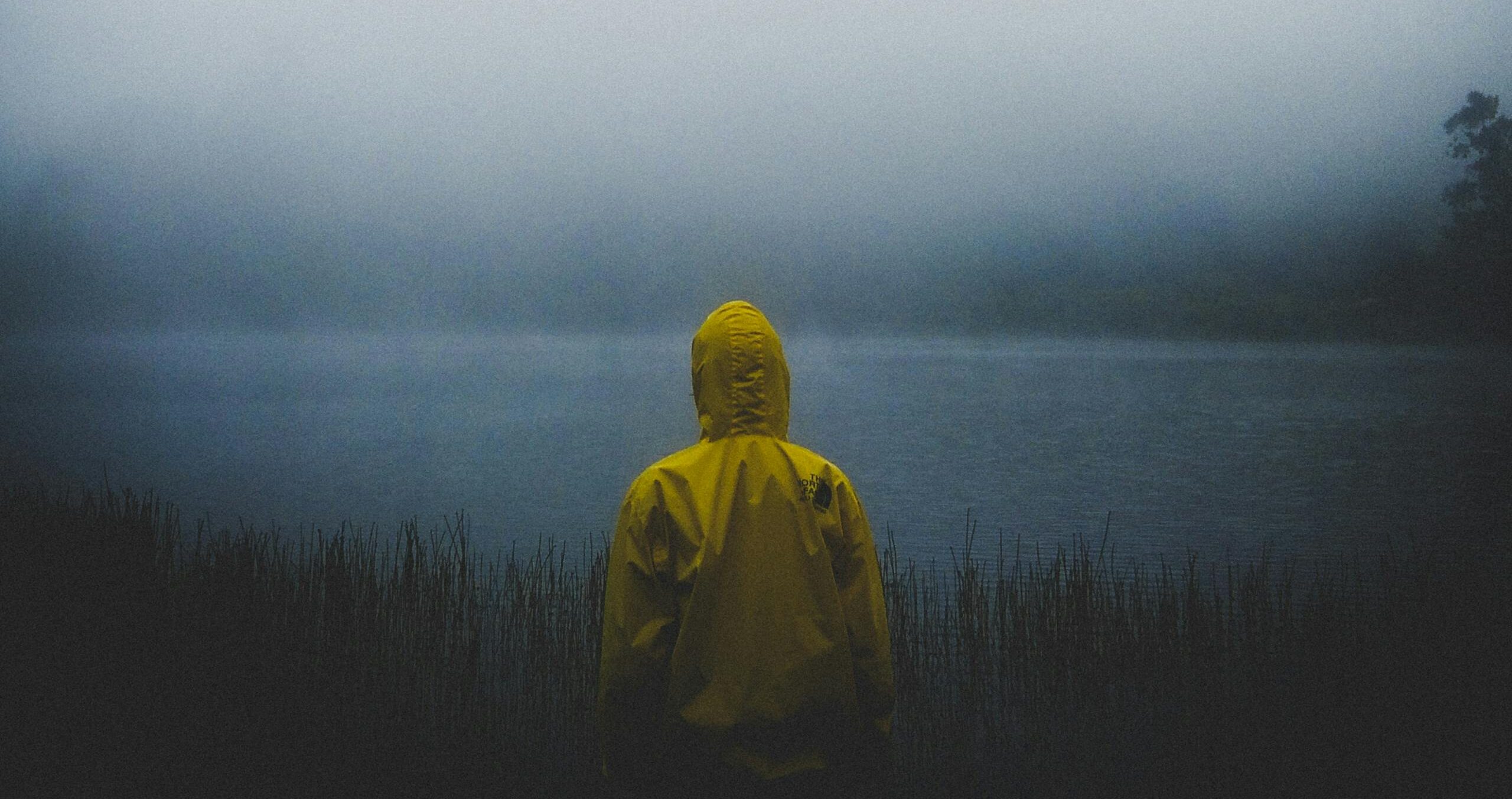 Person in yellow raincoat facing misty lake in Jawa Timur, Indonesia