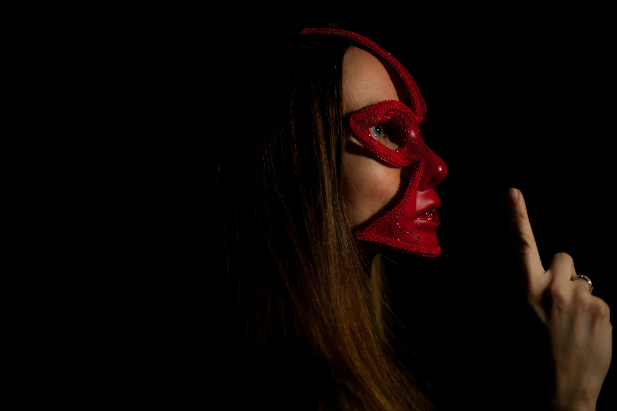 Side view of a woman wearing a red masquerade mask with a black background.