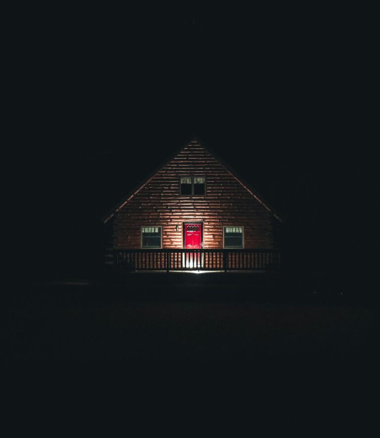 A captivating wooden house with a red door, illuminated at night in a moody setting. Perfect for architectural and real estate themes.