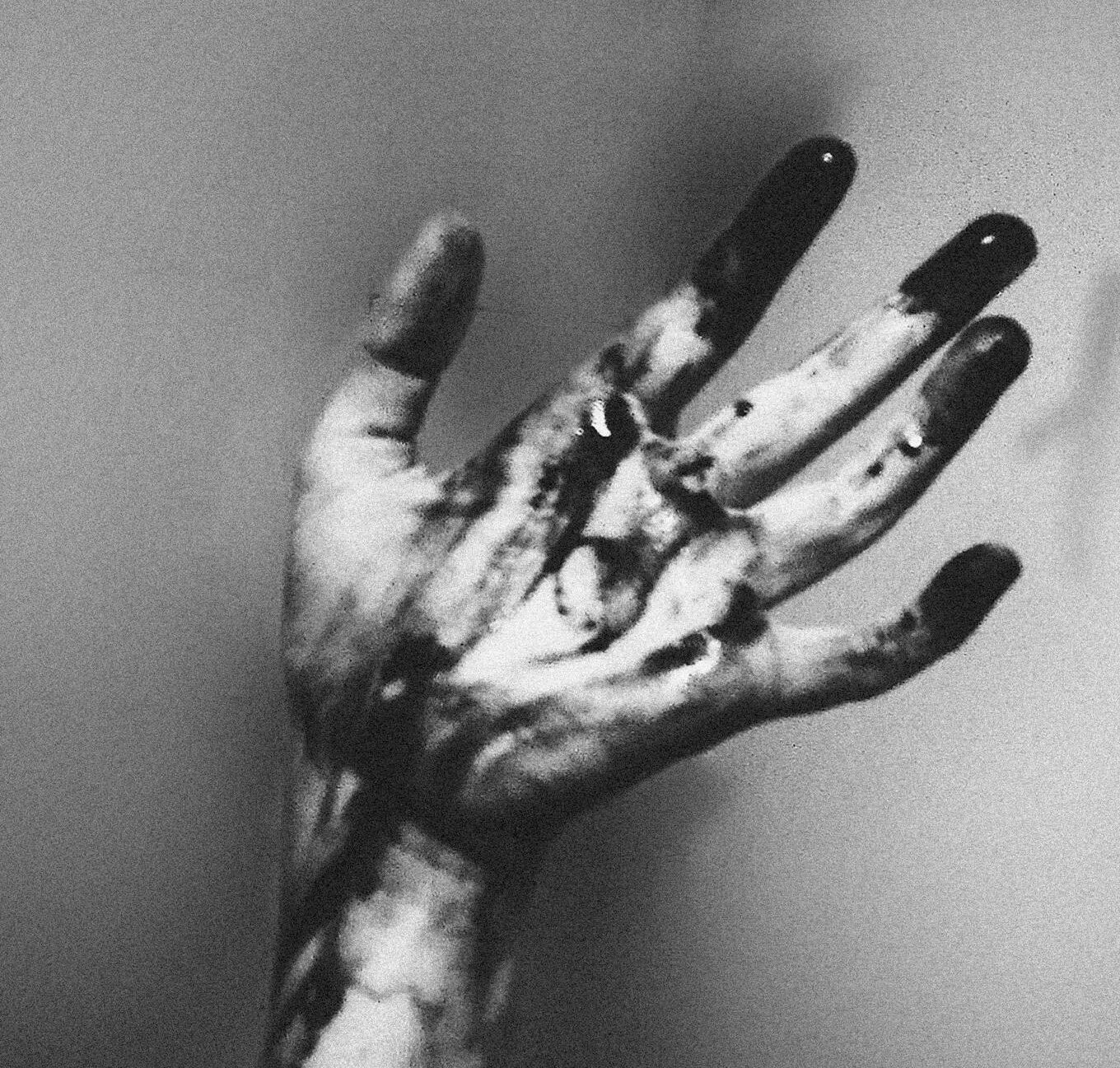 A monochrome image of an outstretched hand with dark liquid dripping, creating a dramatic and moody atmosphere.