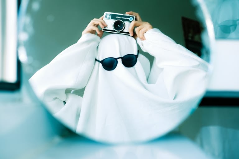 A person in a ghost costume taking a selfie with a vintage camera.