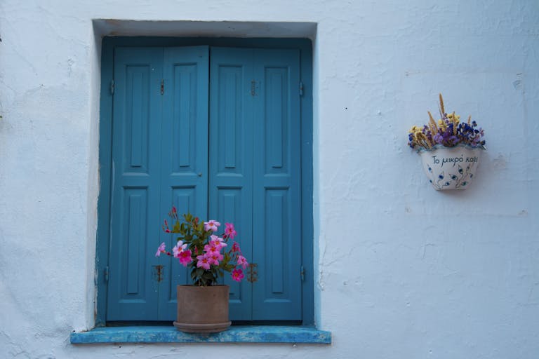 Blue shuttered window with colorful flowers in Skopelos, Greece.