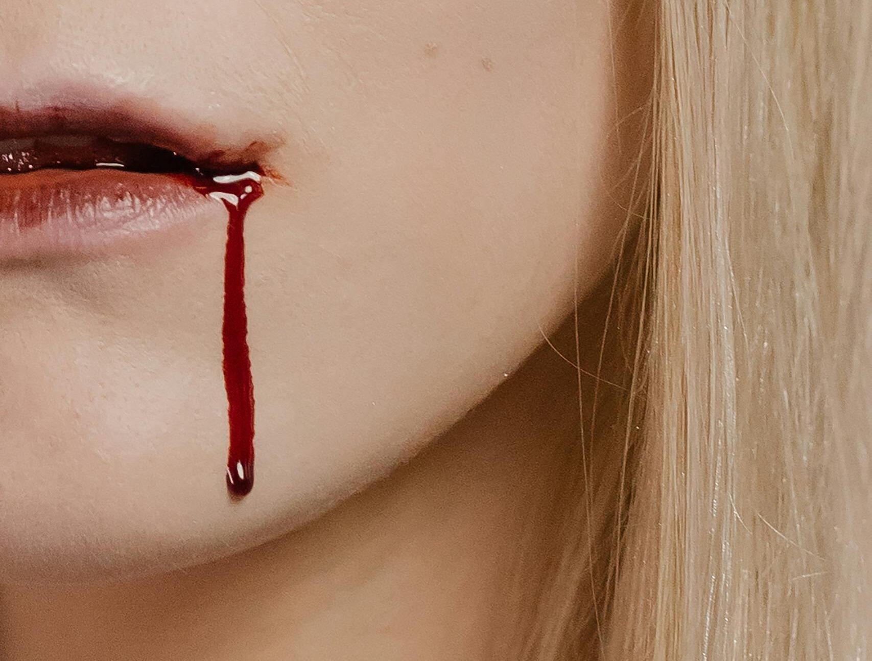 Intense close-up image of a woman with a blonde hairstyle and a dramatic blood effect on her face.
