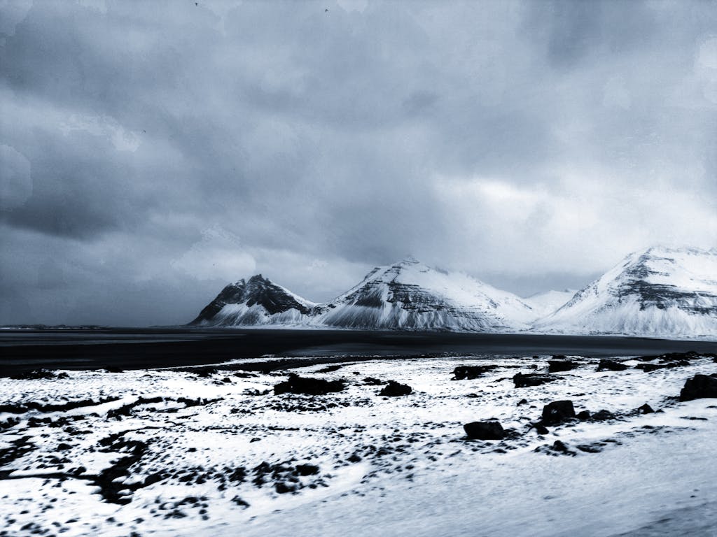 Majestic snowy mountains and coastline under a dramatic cloudy sky in Iceland.