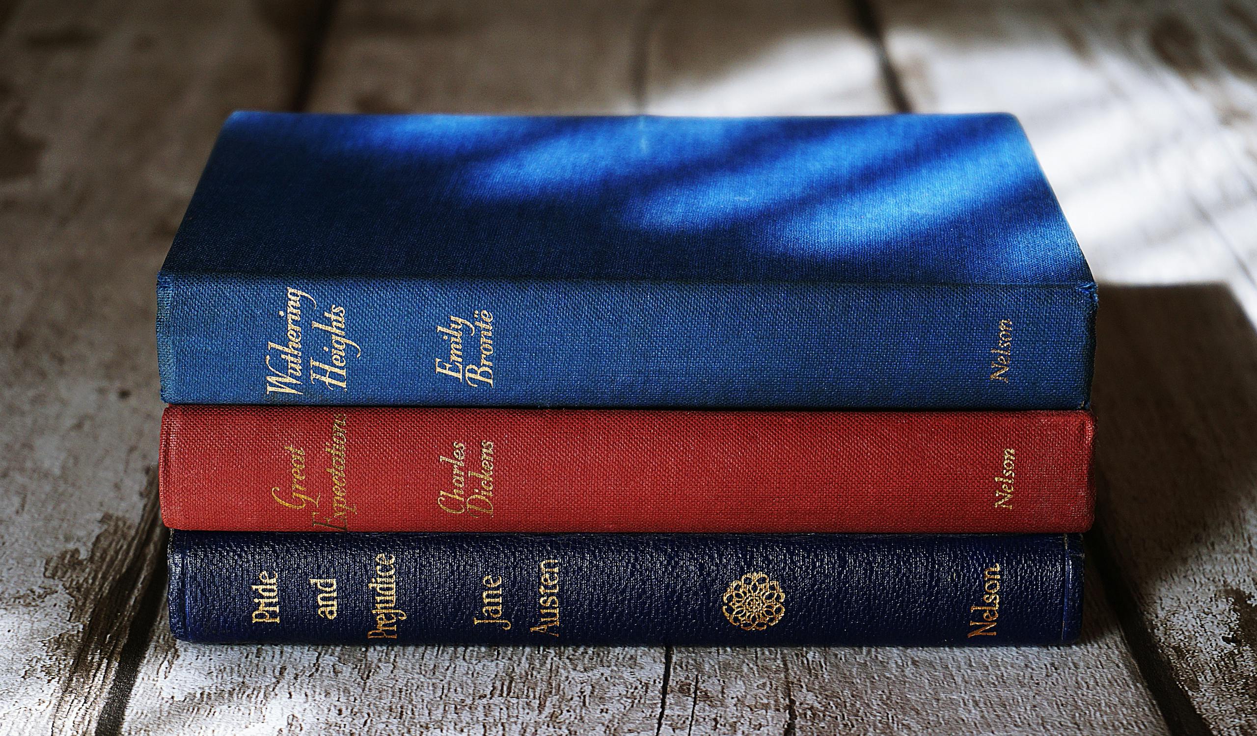 Stacked classics by Brontë, Dickens, and Austen on a wooden surface with dramatic lighting.