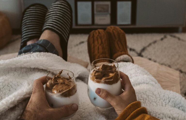 A couple enjoys a cozy movie night with drinks, wrapped in blankets, watching a Harry Potter film on TV.